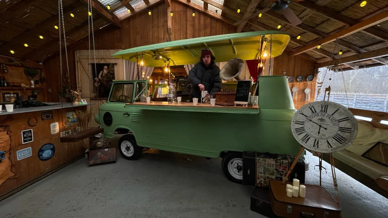Wide view of the green van bar set inside a wooden barn with string lights