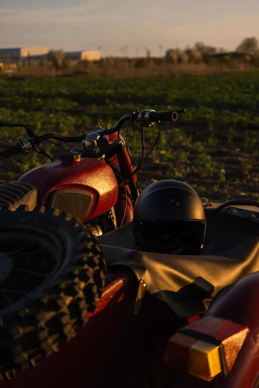 Vintage red motorcycle in a field at golden hour with helmet on the seat
